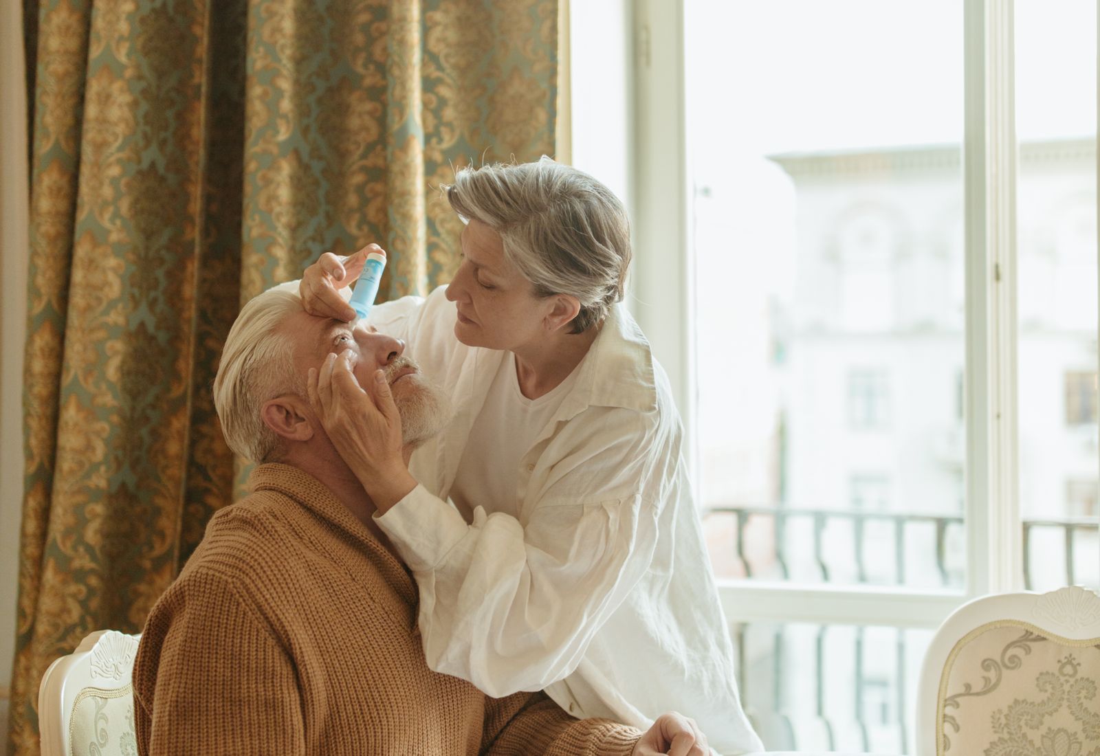 Pflegende Angehörige unterstützt eine ältere Dame am Fenster